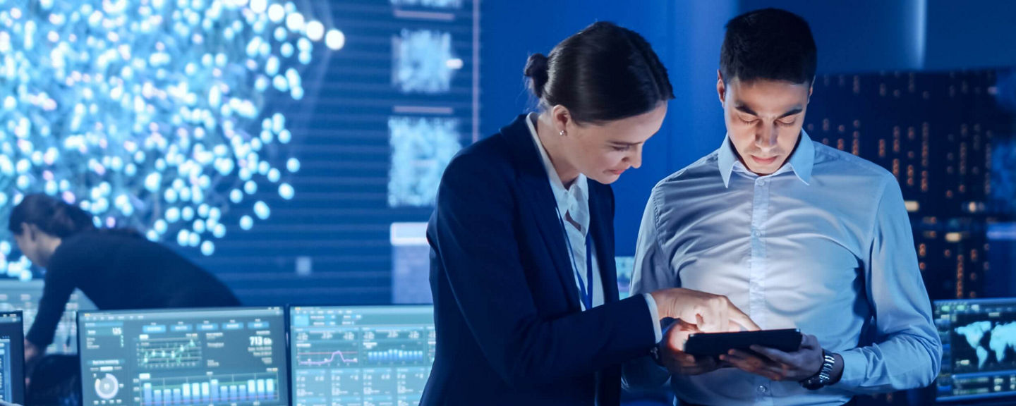 Two business professionals in formal attire collaborating in a high-tech control room filled with digital screens and data displays.