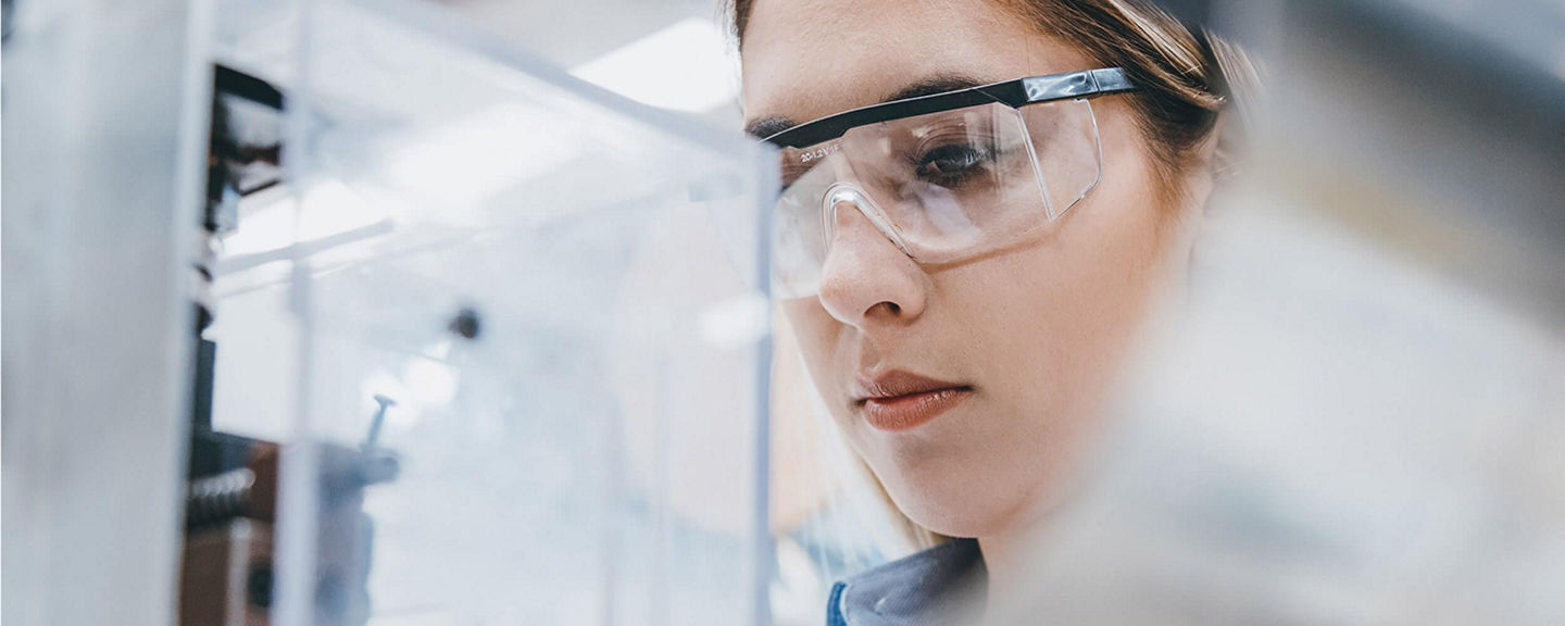 Scientist wearing protective eyewear examining laboratory equipment in a controlled research environment, representing pharmaceutical innovation.