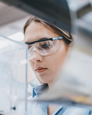 Scientist wearing protective eyewear examining laboratory equipment in a controlled research environment, representing pharmaceutical innovation.
