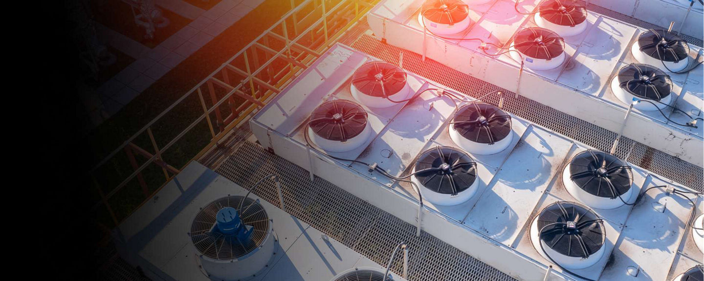 Aerial view of industrial rooftop air conditioning and ventilation systems with large fans and metal piping under bright sunlight.