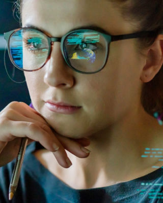 Woman wearing glasses looking at computer screens with data and maps, symbolizing customer communication and technical support.