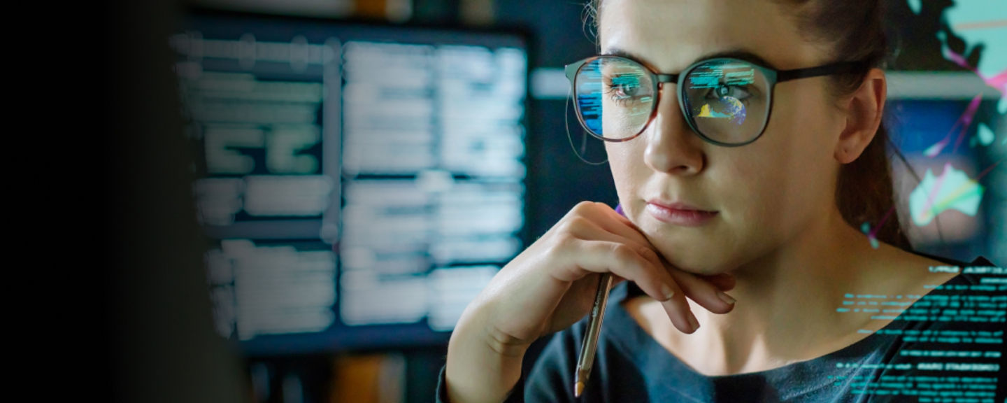 Woman wearing glasses looking at computer screens with data and maps, symbolizing customer communication and technical support.