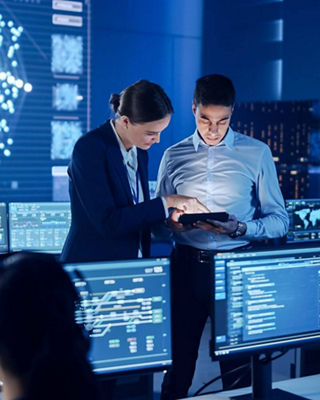 Two business professionals in formal attire collaborating in a high-tech control room filled with digital screens and data displays.