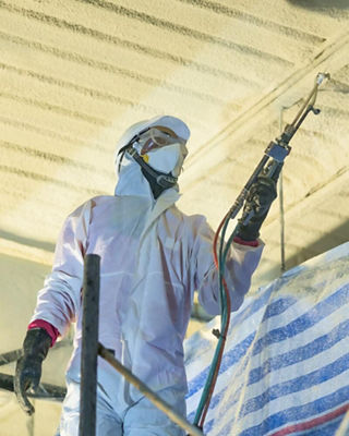 Worker in protective gear spraying insulation foam on a ceiling inside a construction site, representing energy-efficient building insulation.