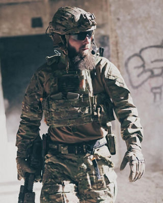 Soldier in tactical gear and helmet with communication headset standing in a low-light environment, representing modern defense operations.