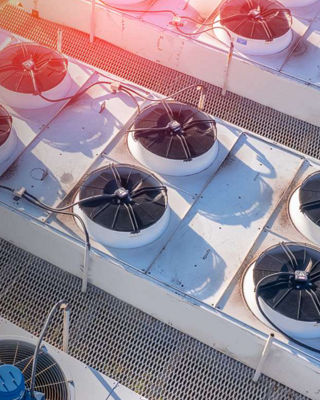 Aerial view of industrial rooftop air conditioning and ventilation systems with large fans and metal piping under bright sunlight.