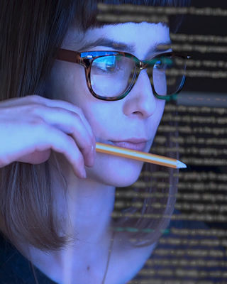 Focused professional woman wearing glasses working on a computer surrounded by lines of code, representing digital talent and career opportunities in technology.