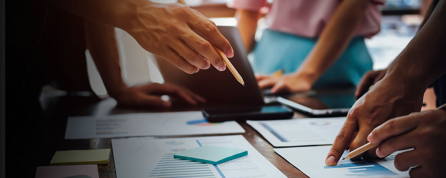 Business professionals collaborating around a desk covered with documents, graphs, and charts during a meeting.