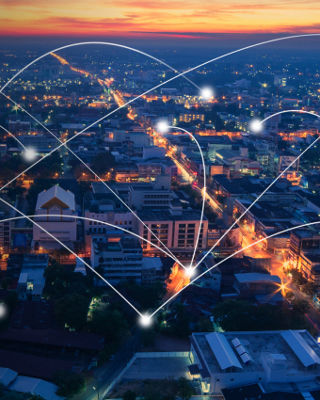 Aerial view of a brightly lit city at dusk with glowing connection lines symbolizing global communication and network connectivity.